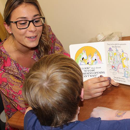 A speech language pathologist student reads to a young boy out of a book.